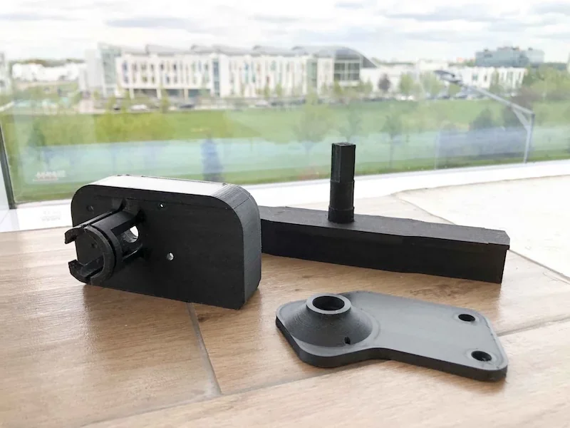 Anisoprint Composer A3 parts on a wooden surface with a cityscape view through a window in the background.