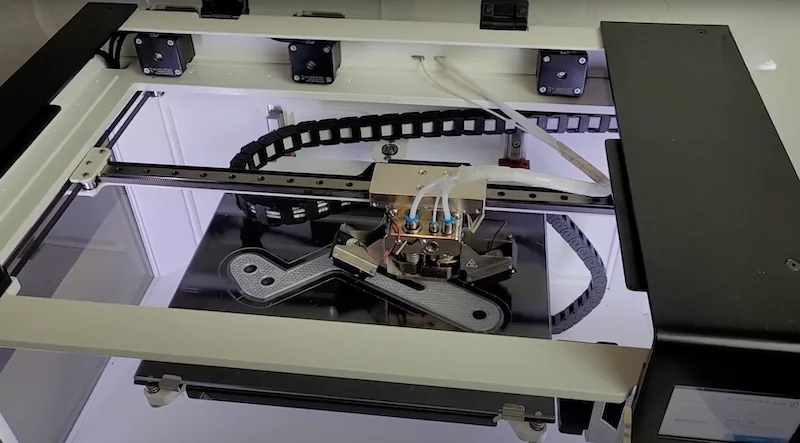 Anisoprint Composer A3 3D printer creating composite parts with visible extruder and printing bed setup within a sleek, modern enclosure.