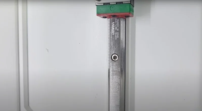 Anisoprint Composer A3 linear rail close-up, showing metal rod with green and red components against a white background, highlighting precision engineering.