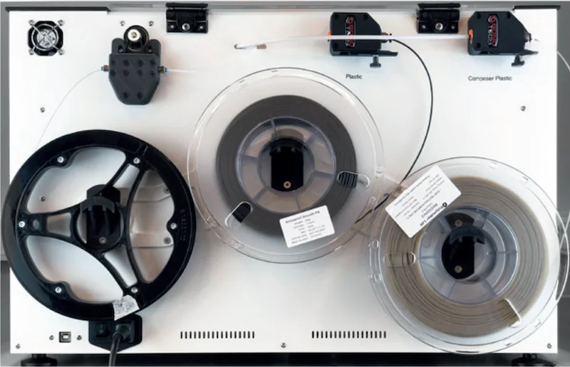 Anisoprint Composer A3 with filament spools and a printed wheel part, featuring labeled plastic and composite lines on a white background.