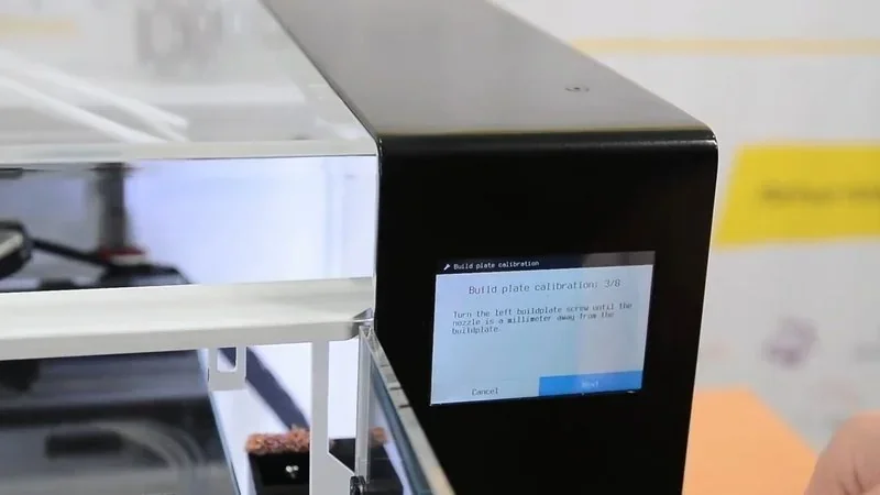 Anisoprint Composer A4 3D printer with display showing build plate calibration; enclosed print area visible.