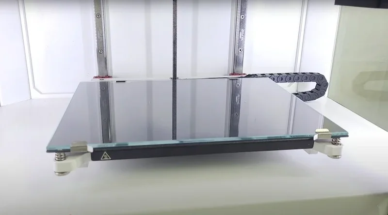 Anisoprint Composer A4 3D printer bed with a flat, reflective glass surface in a white frame, showcasing precise, clean design for part creation.