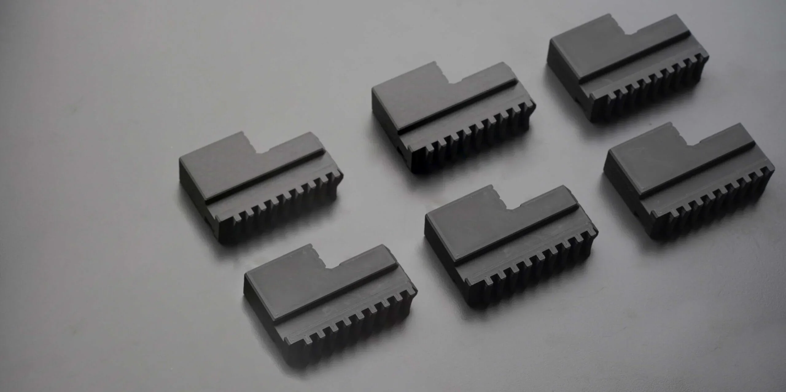 Six black parts with ridges and notches, created by Anisoprint Composer A4, arranged on a gray surface.