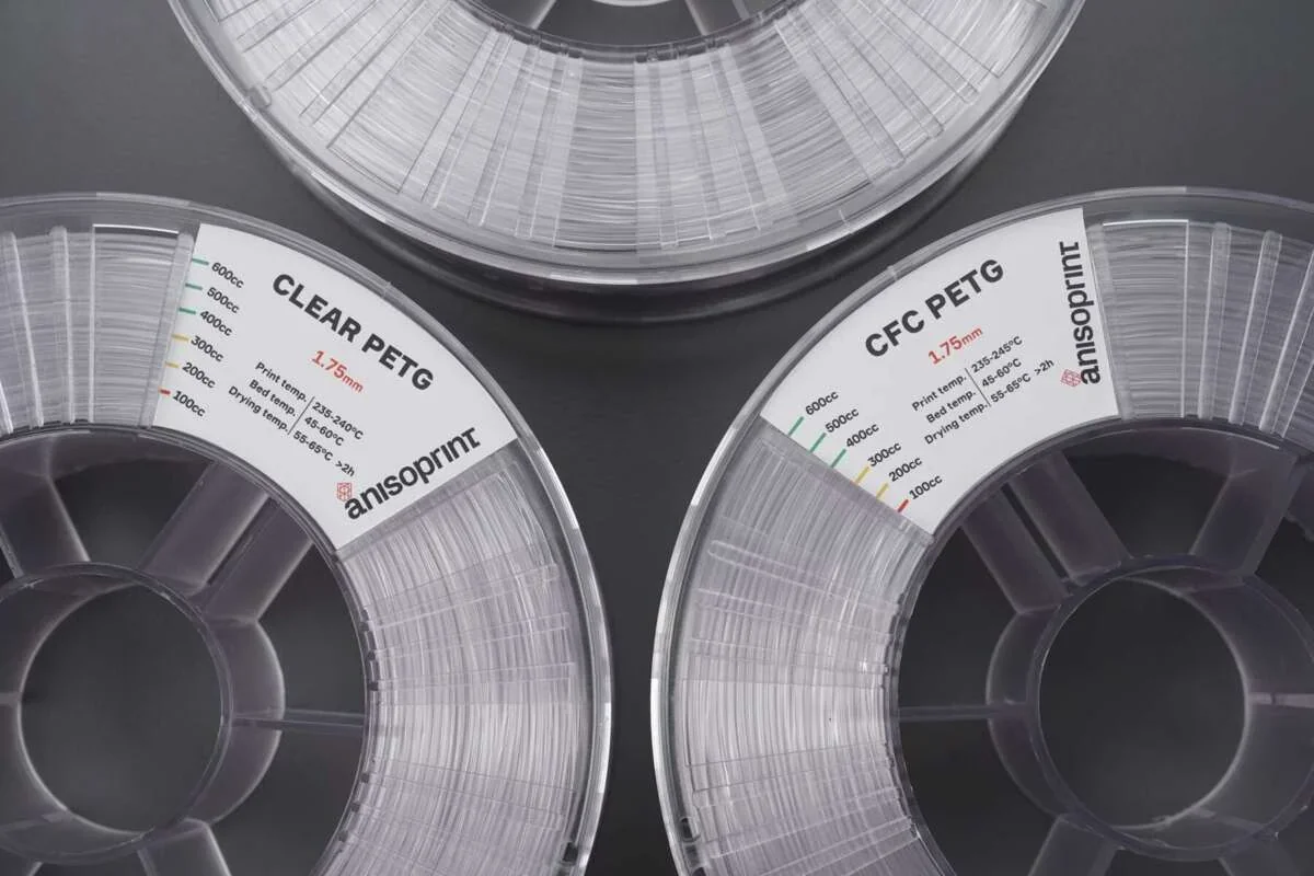 Anisoprint Composer A4 PETG spools, labeled CLEAR and CFC PETG, on a gray background, showcasing filament for 3D printing.