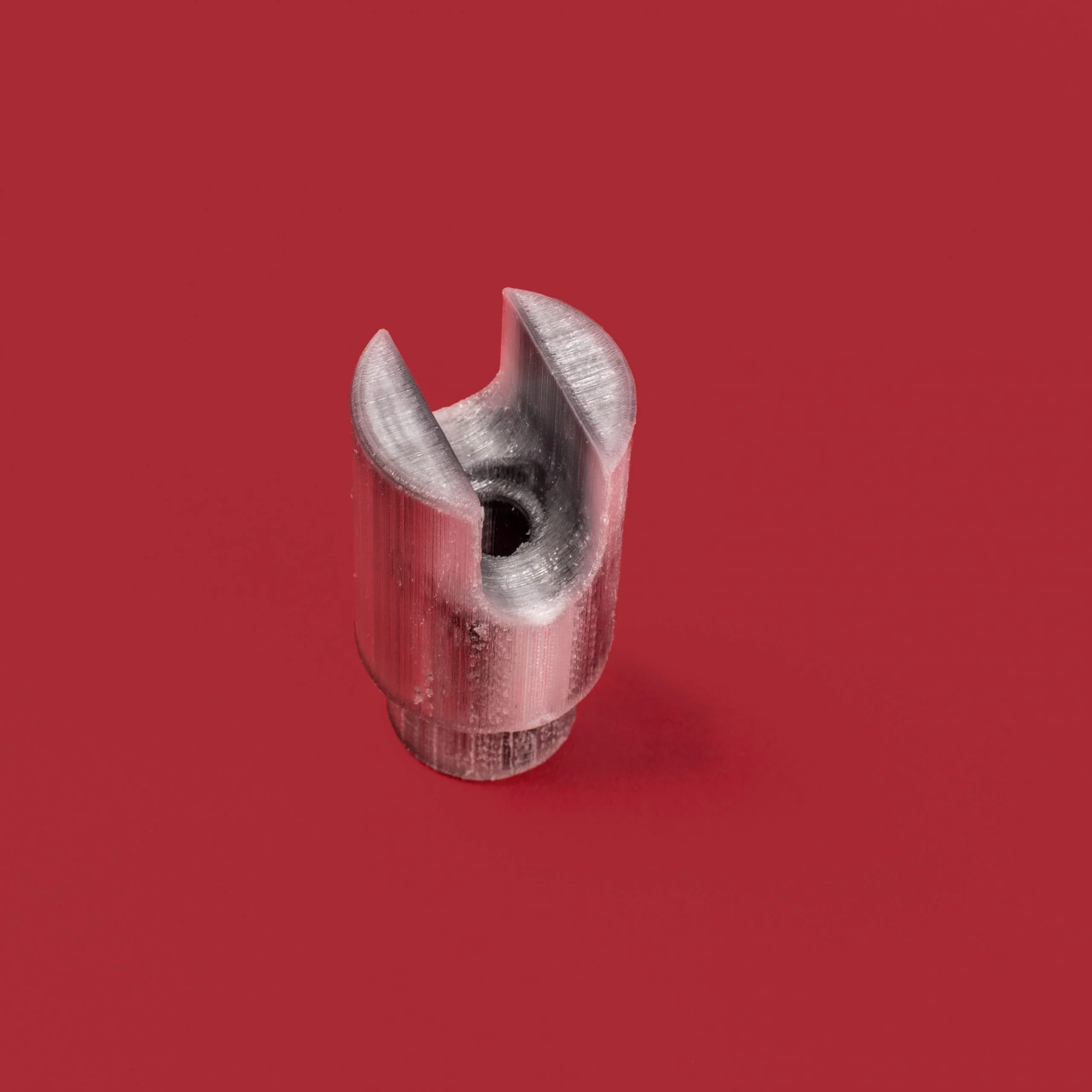 Metallic 3D-printed part made by Anisoprint Composer A4 on a red background, featuring a cylindrical shape with an open slot and hollow center.