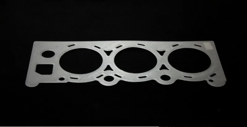 Apium P400 3D-printed gasket on black background, featuring circular and rectangular cutouts, illustrating precision engineering.
