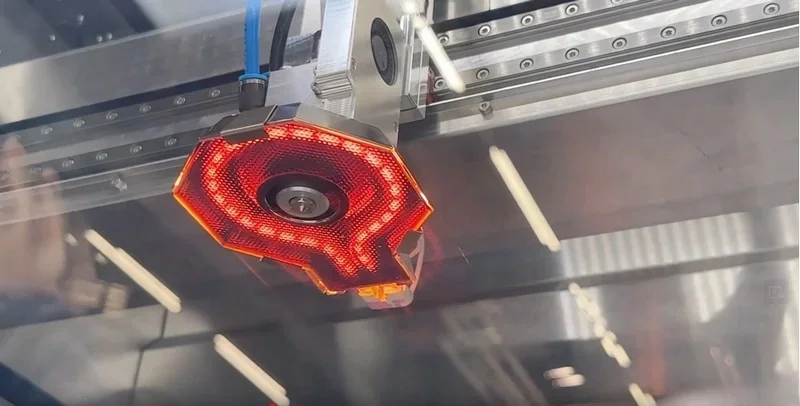 Apium P400 3D printer nozzle with glowing red light inside industrial enclosure, displaying metallic framework and linear rails.
