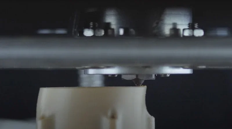 Apium P400 3D printer nozzle depositing material onto a part, showcasing precision and industrial design elements in a professional setting.