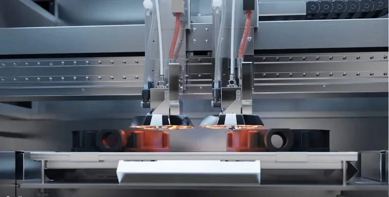 Apium P400 3D printer with dual extruders fabricating complex black components; metallic frame highlights precision engineering.