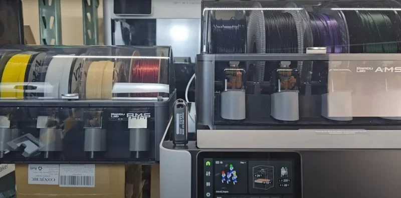 Bambu h2d 3D printer with transparent filament cases, multiple spools, and touchscreen interface, showcasing advanced printing capabilities in a workshop.