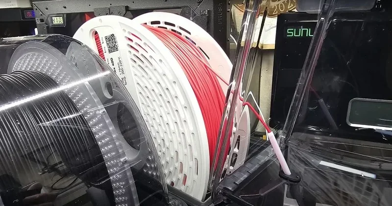 Bambu H2D 3D printer with red and black filament spools inside a transparent enclosure, showcasing high-quality manufacturing components.