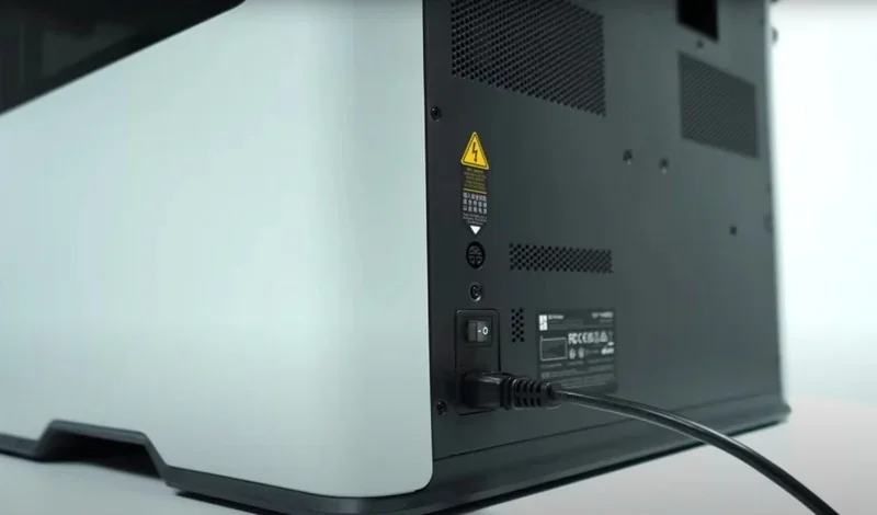 Bambu H2D 3D printer rear view showing power cord connection, ventilation panels, and safety label on black and white casing.