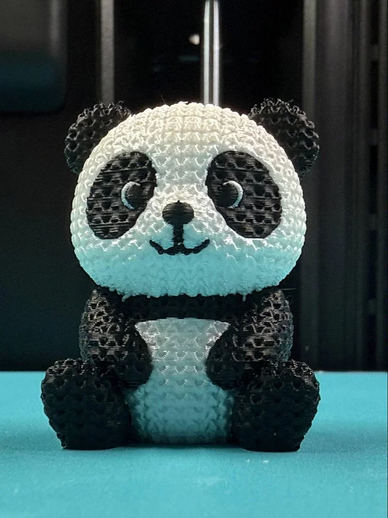 3D-printed panda figurine by Bambu H2D on a turquoise background, showcasing detailed black and white woven texture.