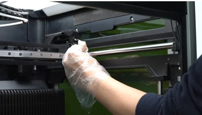 Hand in glove cleaning Bambu Lab H2D Pro 3D printer interior, showing detailed printer components and maintenance setup.