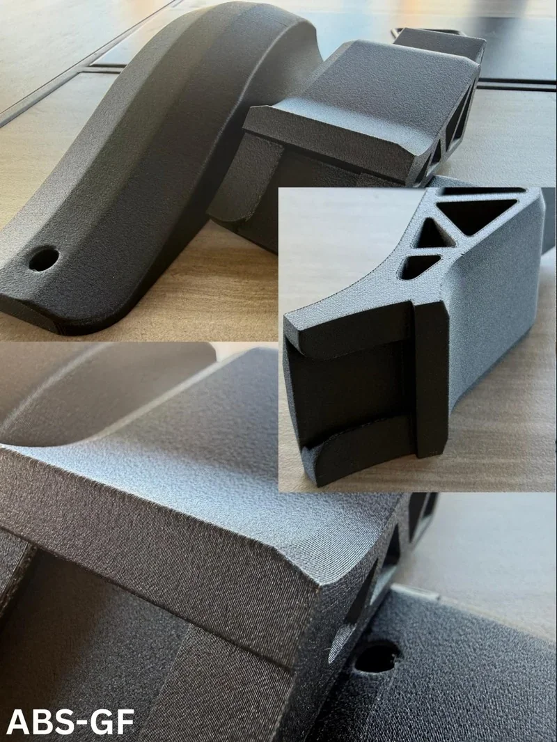 3D-printed black parts by Bambu Lab H2S on wood surface, showcasing textured ABS-GF material close-up.