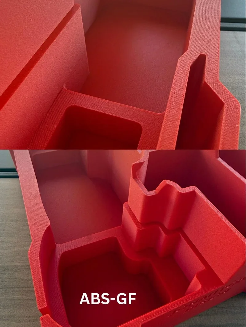 Red 3D-printed parts made with Bambu Lab H2S, showing intricate structures and smooth textures, labeled ABS-GF, on a wooden surface.