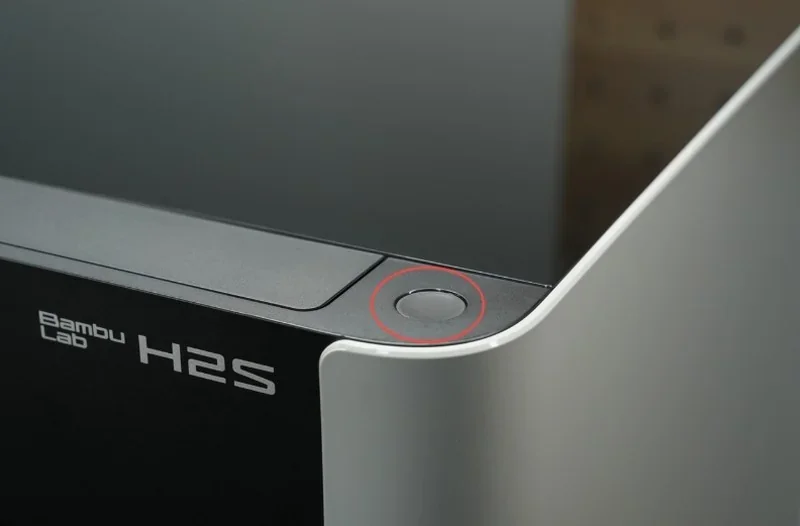 Bambu Lab H2S 3D printer detail showing sleek design, power button highlighted, and branding on the machine in a modern setting.