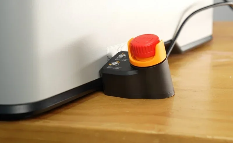 Bambu Lab H2S 3D printer on wood surface, featuring a red emergency stop button with clear labels and secure power cable connection.