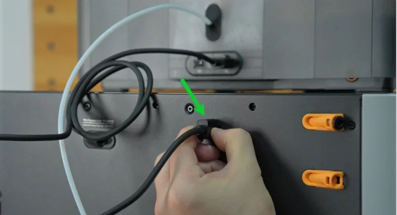 Hand connects cable to Bambu Lab H2S 3D printer, marked by green arrow; gray and orange components visible, focus on assembly detail.