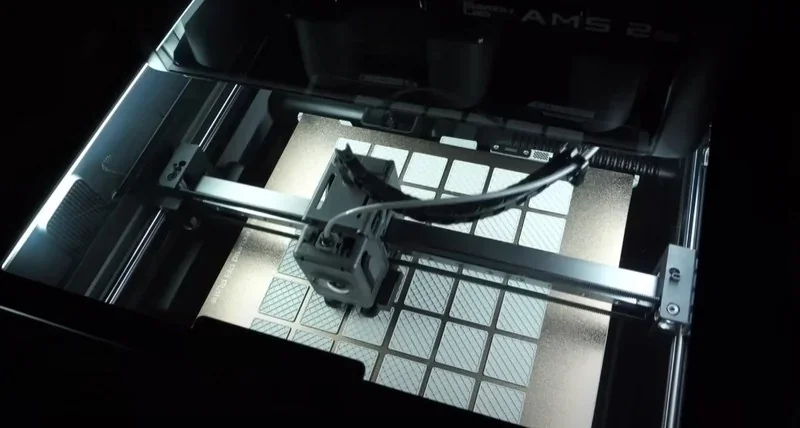 Bambu Lab H2S 3D printer working, showing its print head creating a patterned grid design on a metallic surface in a well-lit interior.