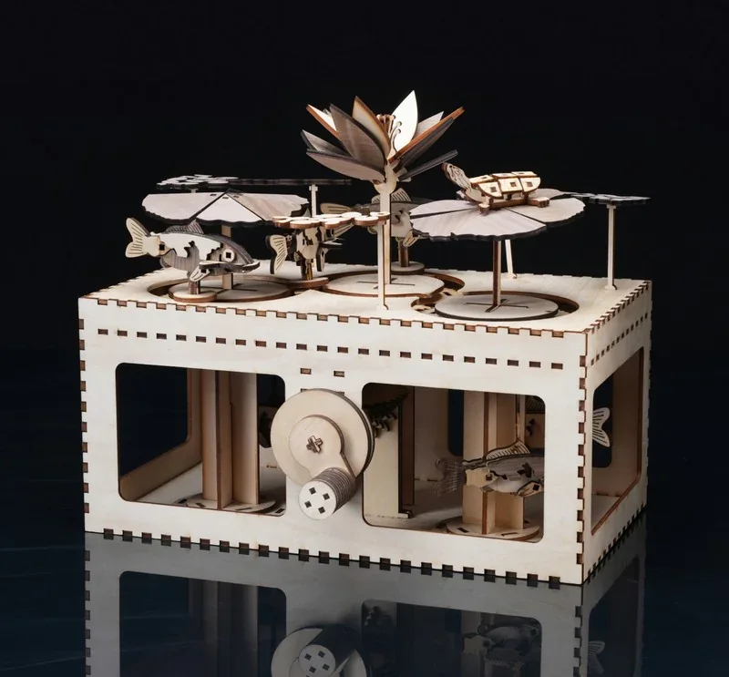 Bambu Lab H2S 3D-printed mechanical box with intricate wooden moving parts, gears, fish, and flower details on a reflective surface.