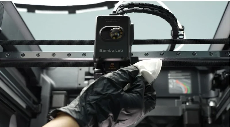 Bambu Lab H2S 3D printer with a hand cleaning the print head inside a technical setting, showcasing intricate components and branded text.