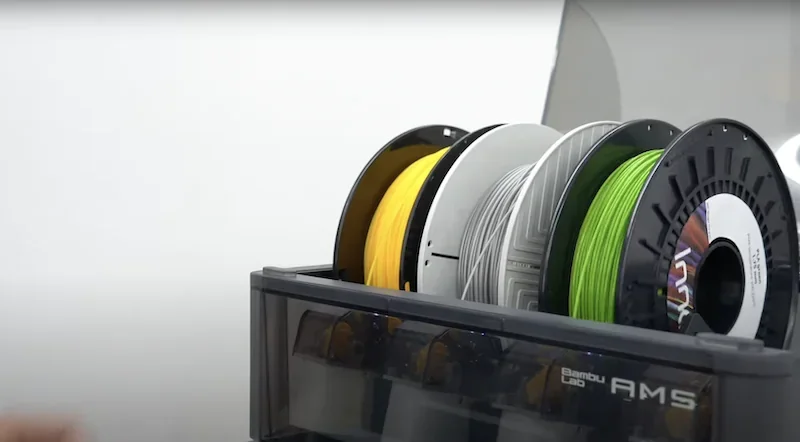Bambu Lab X1 AMS with yellow, gray, and green filament spools, showcasing efficient multi-material 3D printing capability.