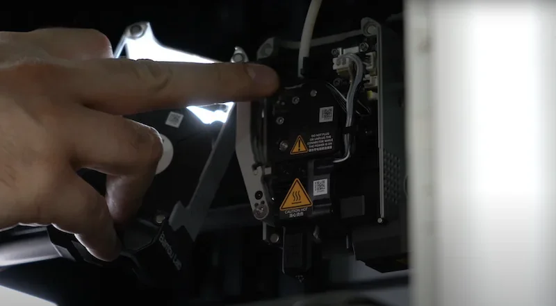 Bambu Lab X1 3D printer with a hand interacting with its internal components, showing intricate mechanical details and branding.