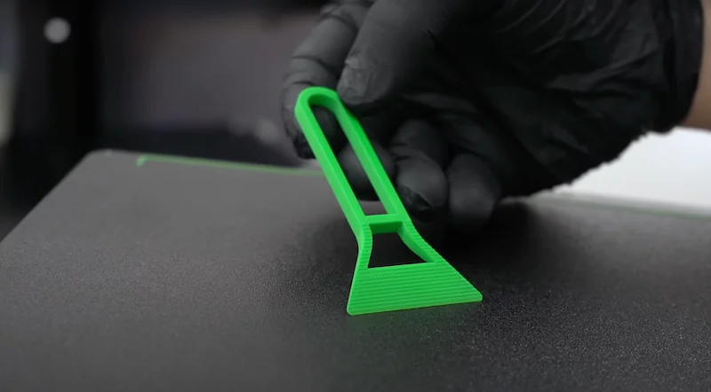 Green 3D-printed tool created by Bambu P1P held by a gloved hand over a textured surface.