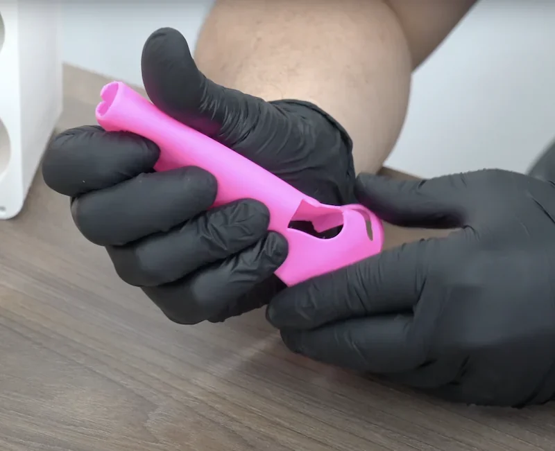 Gloved hands hold a pink 3D-printed part, likely created by Bambu P1P, set on a wooden table.
