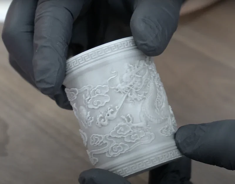 3D-printed ornate cylindrical object with dragon motif, crafted by Bambu P1P, held by gloved hands on wooden surface.
