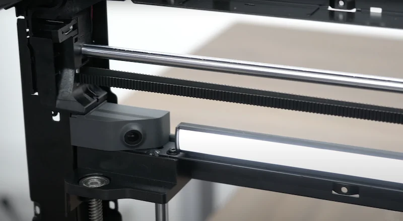 Close-up of Bambu P1P 3D printer's internal mechanism, featuring metal rods, a belt, and components. No branding visible.