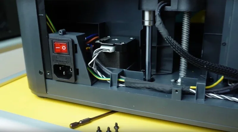 Bambu P1P 3D printer internal view showing wiring, switch, motor, and components on a yellow surface.
