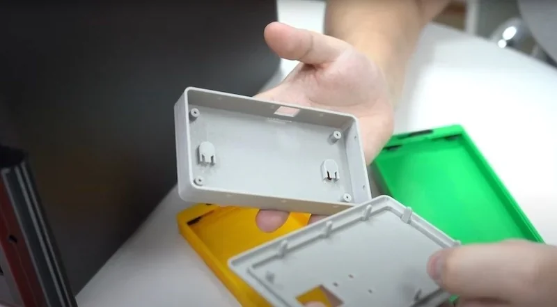 Hands hold colorful 3D printed cases, likely created by Bambu P1S, showcasing precision and detail.