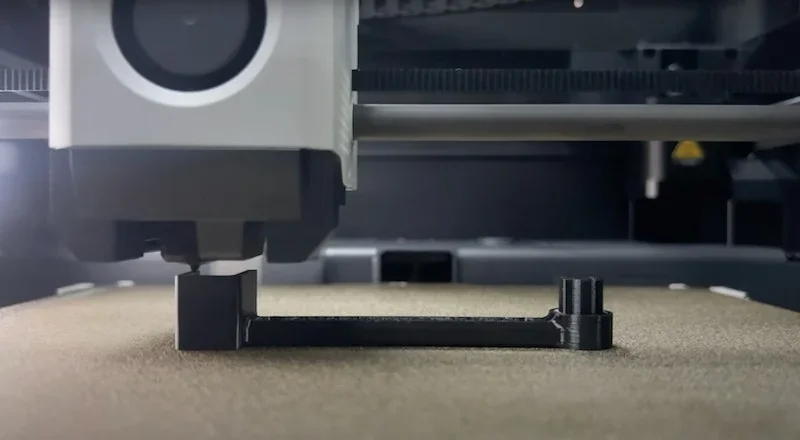 Bambu P1S 3D printer creating a black plastic part on a textured bed, highlighting precision printing technology in action.