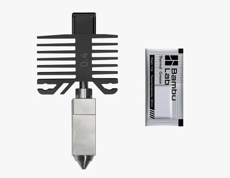 Bambu P1S 3D printer nozzle and thermal grease packet. Nozzle features a black heat sink with metal tip; Bambu Lab branding on grease packet.