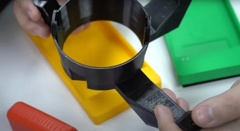 Hands holding a black 3D-printed part created by Bambu P1S, with colorful blocks in the background on a white surface.