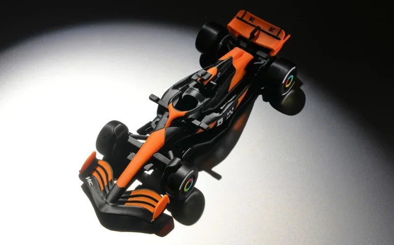 Bambu P2S 3D-printed orange and black race car model on a dark background, showcasing precise detailing and vibrant colors.