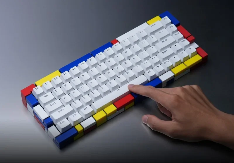 Colorful 3D-printed keyboard housing in primary colors designed with Bambu P2S printer, hand touching a key, showcasing precision and creativity.