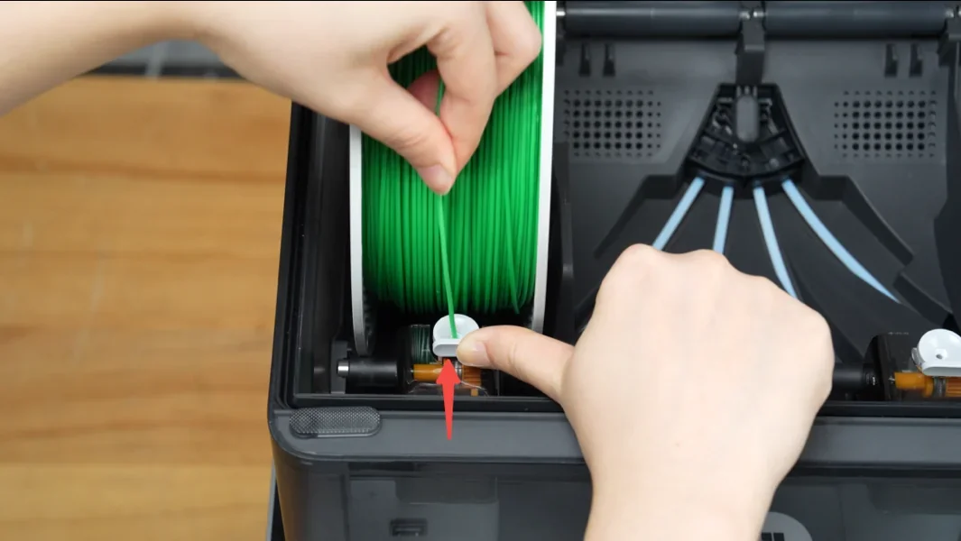 Bambu P2S 3D printer with hands loading green filament spool inside, showcasing setup process and internal components.