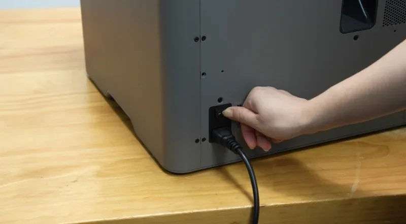 Hand plugging power cable into Bambu P2S 3D printer on a wooden table.