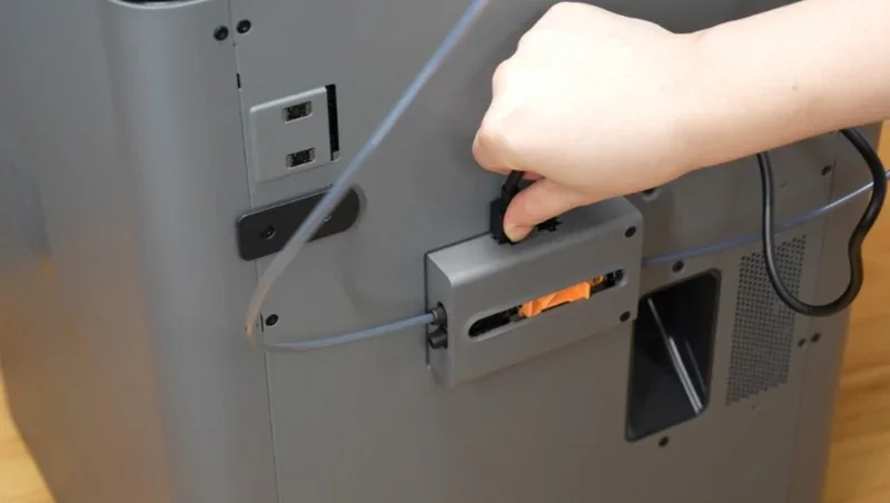 Hand adjusting filament in a Bambu P2S 3D printer, showing gray casing and control ports.