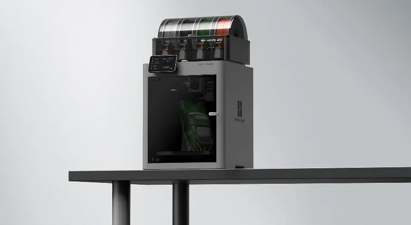 Bambu P2S 3D printer with filament spools on top, on a table. A model truck inside, showcasing printing capabilities.