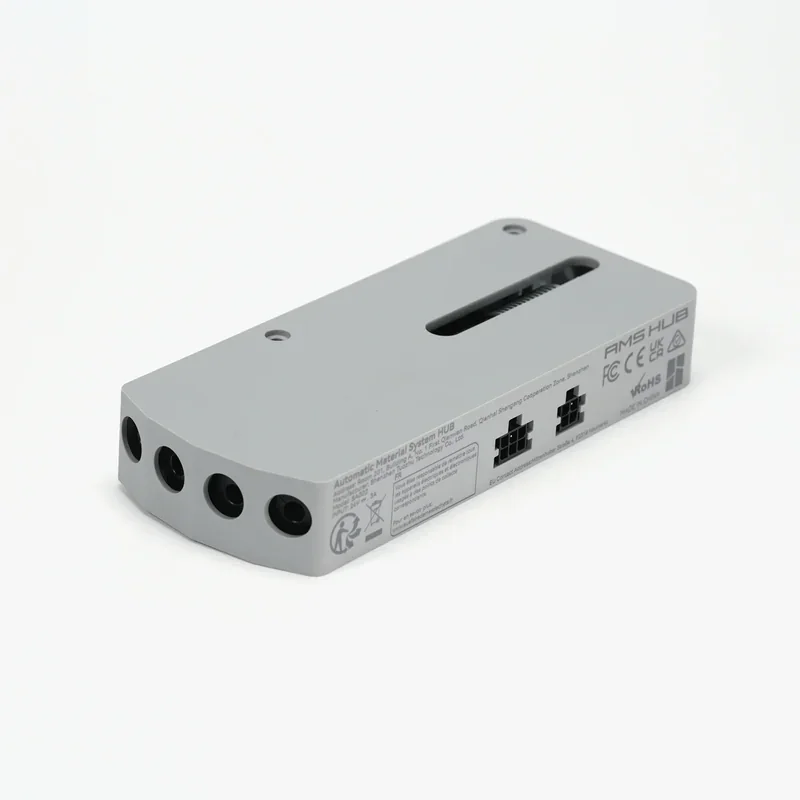 Gray rectangular AMS Hub module with ports and labels on a white background, associated with Bambu X1E 3D printer accessories.