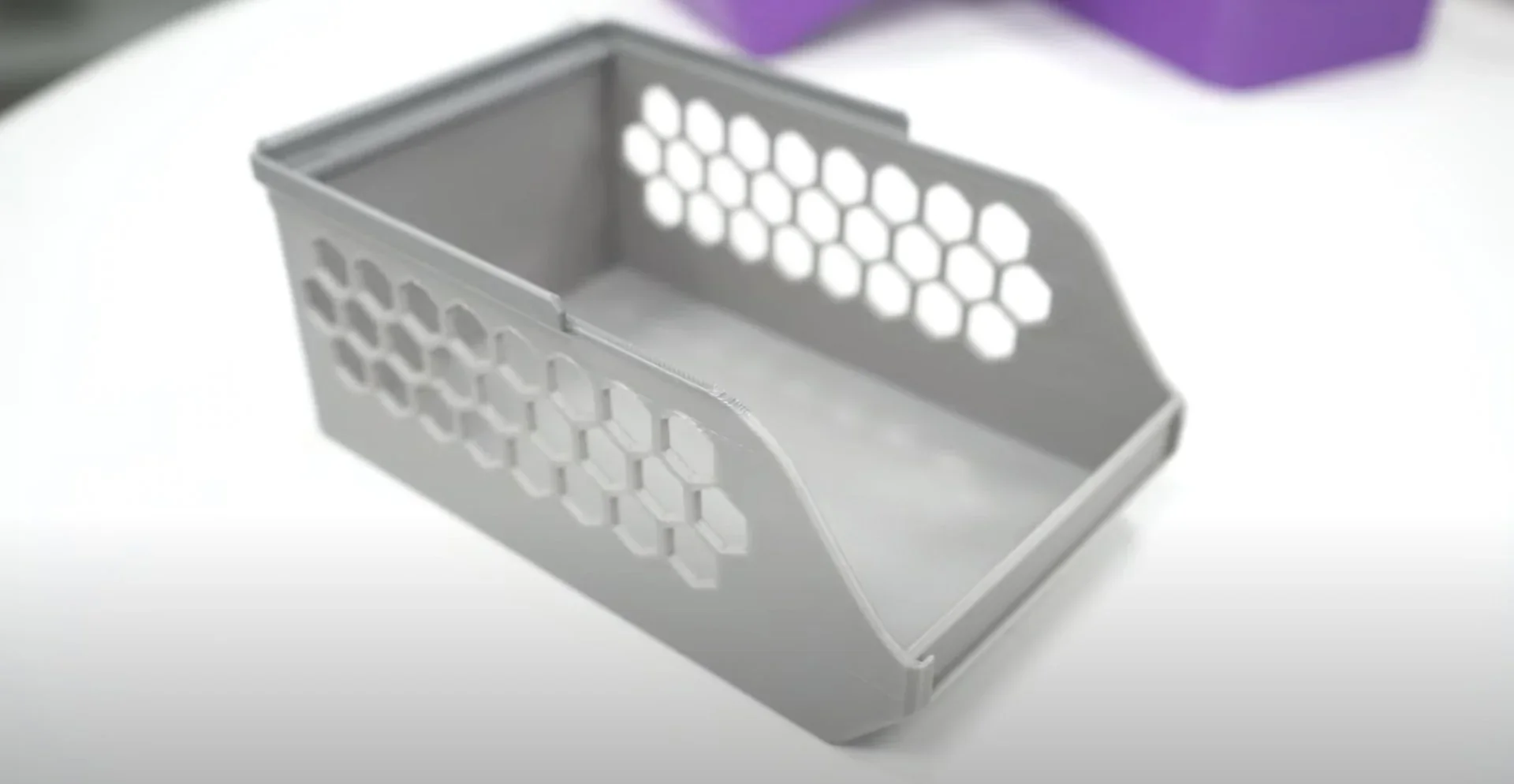 Gray 3D-printed basket with hexagonal cutouts, created by bambu x1e, on a white surface, showing intricate design and function.