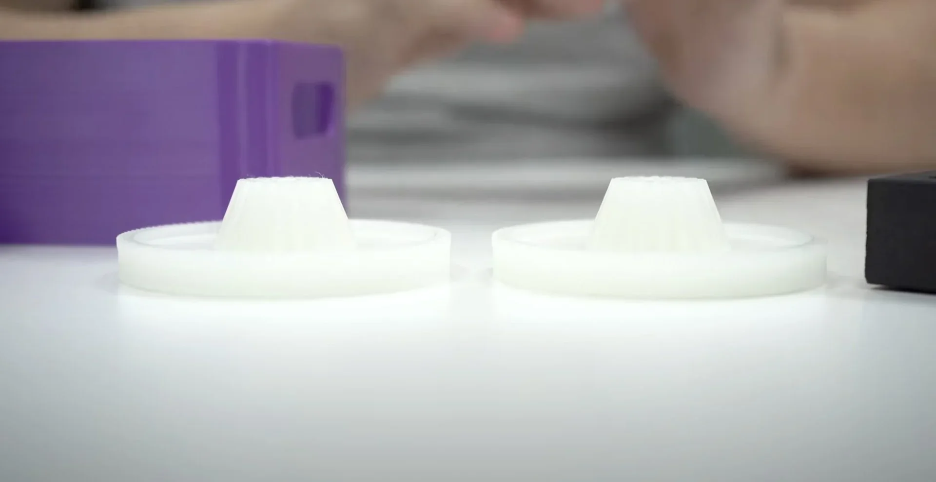 3D printed white gears on a table, created by Bambu X1E, with a blurred purple object in the background.