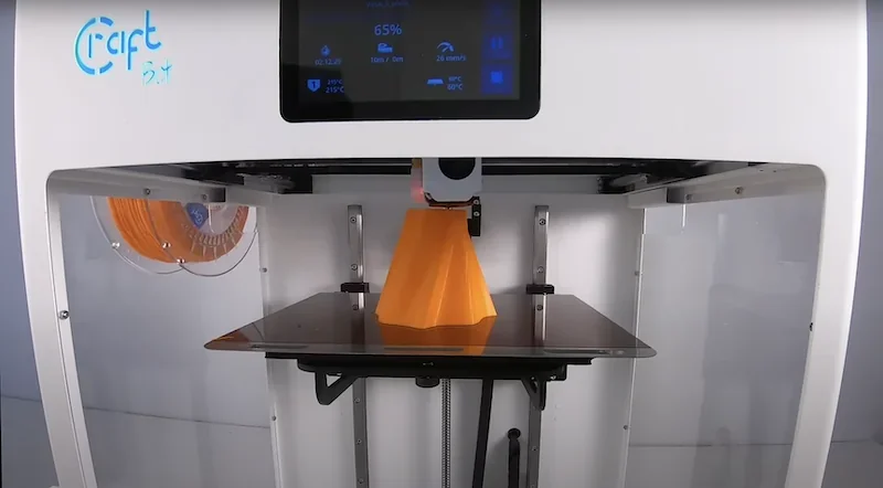 Craftbot Flow IDEX XL 3D printer printing an orange model with visible filament spool and control screen showing progress and settings.