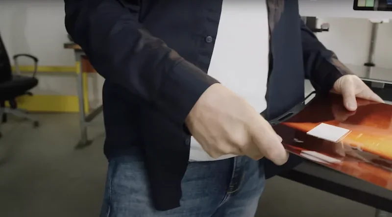 Person holding a 3D printed object created by Craftbot Flow IDEX XL in a workshop setting, wearing casual attire, next to a desk.