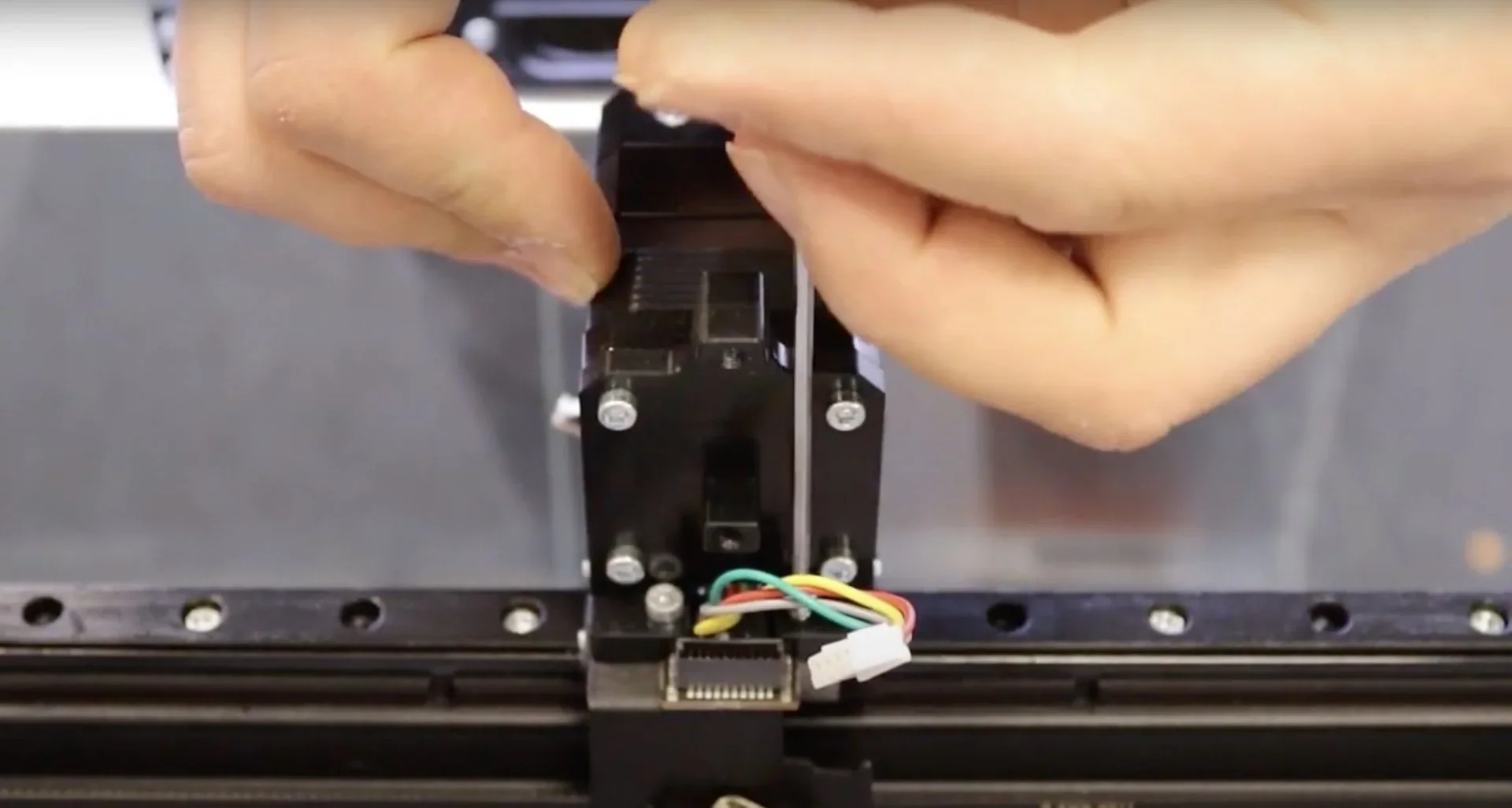 Hands adjusting the Craftbot Flow IDEX XL 3D printer component with wires visible, showcasing part of the assembly or maintenance process.