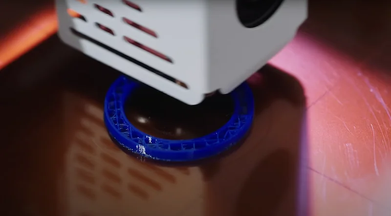Craftbot Flow IDEX XL 3D printer head printing a blue circular design on a red surface, showcasing precise additive manufacturing technology.